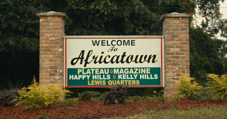 Sign suspended between two brick columns. Welcome to Africatown. Plateau, Magazine, Happy Hills, Kelly Hills, Lewis Quarters