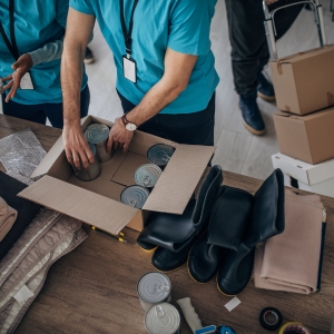 Workers wearing blue t-shirts and lanyard badges packaging can goods and other items in boxes